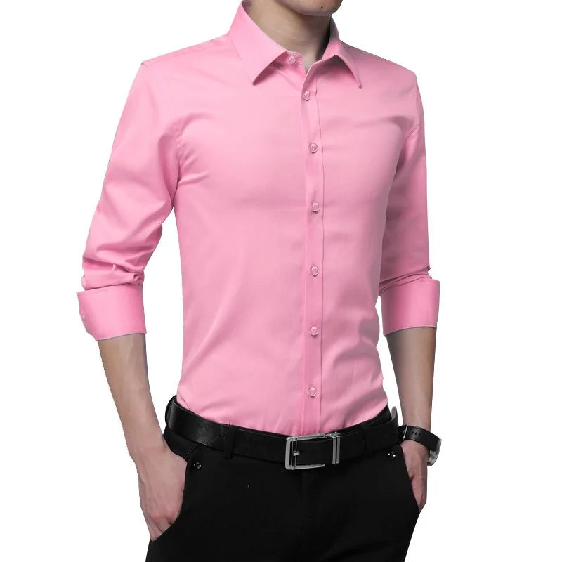 A fashionable man wearing a slim-fit, long-sleeved pink dress shirt with the sleeves rolled up to his elbows. The shirt features a structured collar and matching pink buttons. He pairs the shirt with black dress pants, a black belt with a silver buckle, and a stylish black wristwatch on his left wrist. His hands are casually tucked into his pockets, presenting a confident and polished look.
