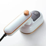 A compact handheld electric iron/garment steamer in white with rose-gold trim, shown with a power cord and a rounded base on a white background.
