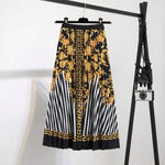 Pleated midi skirt with a gradient design, transitioning from dark black at the waistband to a soft blush pink at the hem, hanging on a black clothing rack next to a vintage-style camera.