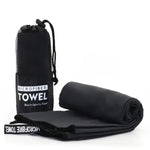 A black microfiber towel folded and rolled beside a black mesh drawstring pouch labeled “MICROFIBER TOWEL (Beach•Sports•Travel)