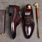 A pair of elegant burgundy leather loafers with a glossy finish. The shoes feature gold-toned metal horsebit detailing across the uppers and are displayed with wooden shoe trees inserted. They have a sleek, elongated silhouette with subtle stitching along the toe cap. The loafers are placed on a dark surface, partially framed by a wooden picture frame, emphasizing their classic and sophisticated style.