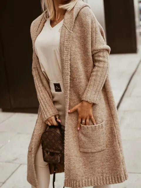 Person wearing a long beige cardigan over a white top, holding a brown bag.