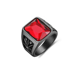 A bold, dark-colored men's ring featuring a large, square-cut red gemstone at the center, with intricate black detailing on the sides. The design suggests a robust and striking style.