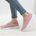Person wearing pink slip-on sneakers with a chunky sole, a gold crown emblem on the upper, and a small gold zipper detail on the side, paired with blue jeans and an ankle bracelet.