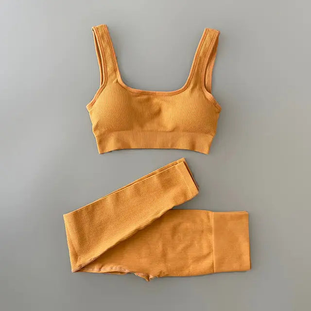 Black ribbed sports bra and matching high-waisted leggings set laid flat on a neutral gray background. The outfit is designed for activewear or athleisure, featuring a scoop neckline and wide straps on the bra.