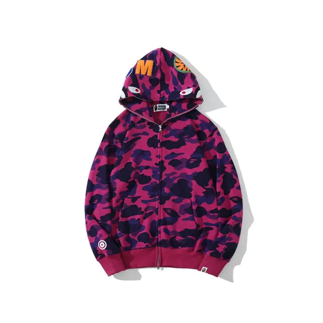 Camouflage zip-up hoodie in tan and dark green with a shark-face design on the hood, including embroidered eyes and orange lettering.