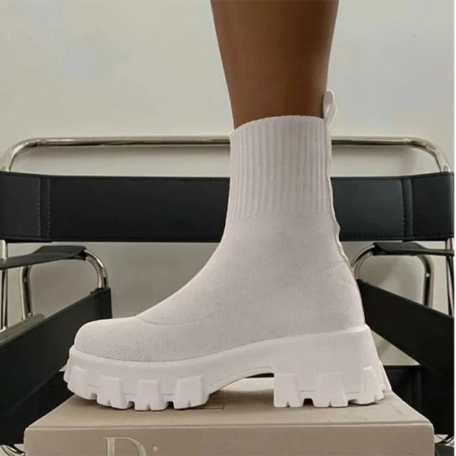 A pair of chunky lavender sock boots with thick platform soles and ribbed knit uppers, displayed on a gray tiled floor against a light-colored wall.