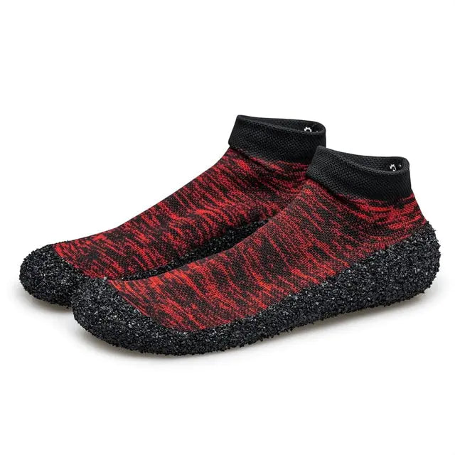 A pair of snug slip-on water shoes with a sock-like upper in a red and black heathered knit pattern. They feature black ankle cuffs and textured black rubber-coated soles that wrap around the sides for added grip and protection.