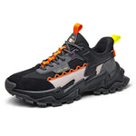 Black chunky trainer with orange laces, grey panels and rugged tread sole.