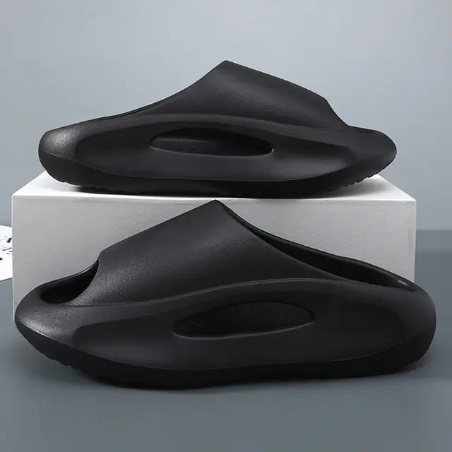 A pair of stylish black slip-on sandals with purple cushioned insoles, featuring cutout designs on the sides and toes, displayed on a white surface next to stacked books.