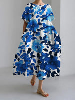 Woman wearing a loose-fitting, white midi dress with short sleeves, featuring bold red-orange floral prints accented with blue centers, paired with flat sandals.