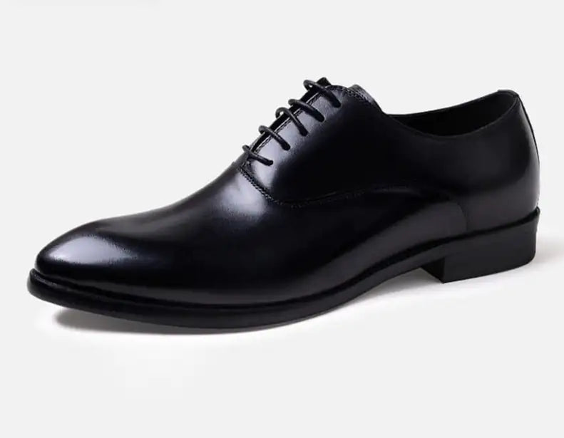 A pair of elegant burgundy leather loafers with a glossy finish. The shoes feature gold-toned metal horsebit detailing across the uppers and are displayed with wooden shoe trees inserted. They have a sleek, elongated silhouette with subtle stitching along the toe cap. The loafers are placed on a dark surface, partially framed by a wooden picture frame, emphasizing their classic and sophisticated style.