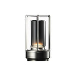 Compact modern lantern-style table lamp with a black cylindrical inner shade inside a rectangular metal frame, emitting a warm glow from the base on a white background.
