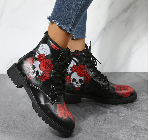 Black boots with skull and rose design worn with jeans on a gray floor.