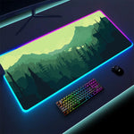 A large RGB gaming mouse pad with a vibrant, glowing border, featuring a forest landscape in the background. A compact rainbow-colored mechanical keyboard and a black gaming mouse are placed on the mat. The desk is illuminated with soft lighting.