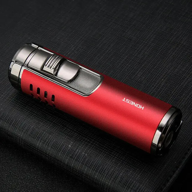 A close-up product photo of a compact red rechargeable lighter (or torch-style igniter) lying on a dark textured fabric surface. It has metallic silver ends and a silver top section with a sliding ignition switch, plus small ventilation slots on the side. The brand name “HONEST” is printed in white on the red body.