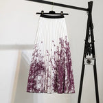 Pleated midi skirt with a gradient design, transitioning from dark black at the waistband to a soft blush pink at the hem, hanging on a black clothing rack next to a vintage-style camera.