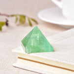 Small translucent green crystal pyramid placed on the corner of a light-colored book, with a soft blurred background.