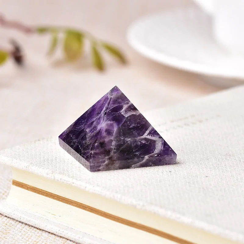 Small polished purple amethyst pyramid with white veining, resting on a closed book against a soft, light background.