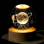 A glowing globe featuring a girl floating around a planet with a ring, surrounded by stars, sitting on a wooden base.