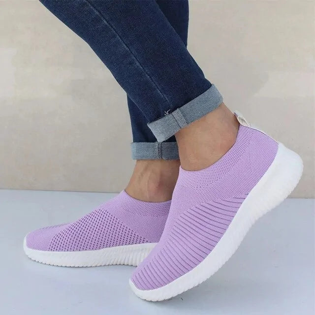 Light purple slip-on knit sneakers with thick white soles, worn with rolled-up blue jeans.