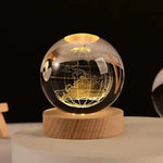 Glowing crystal globe lamp etched with a world map and latitude/longitude lines, resting on a round wooden base in a dark setting.