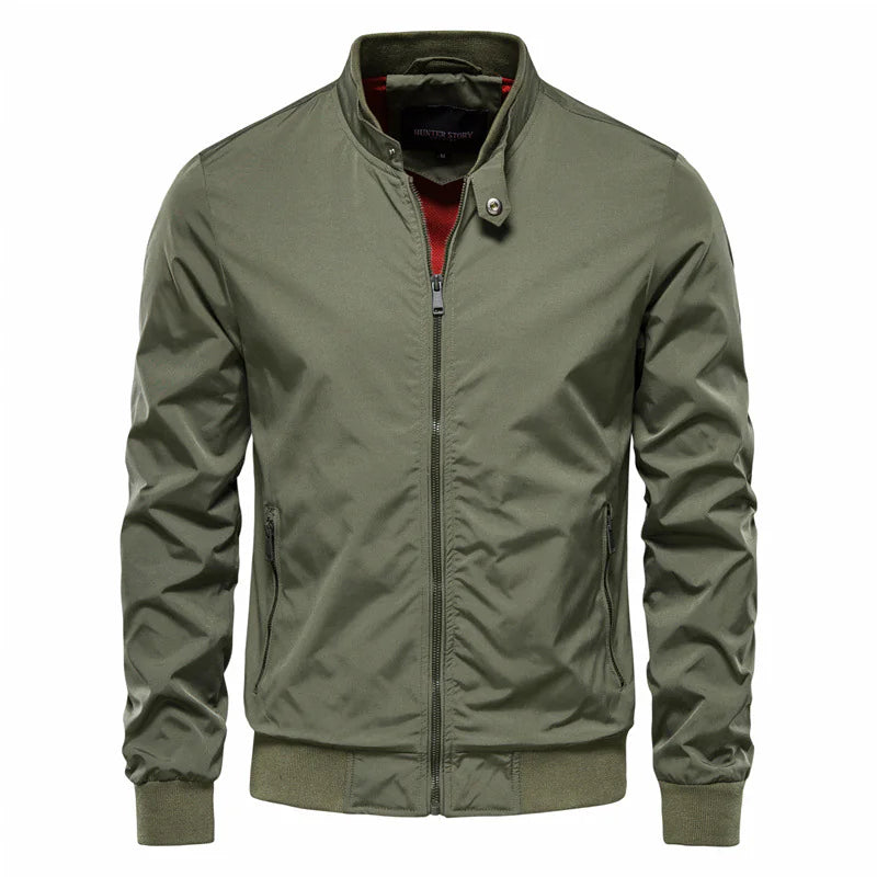 A stylish olive green bomber jacket with a zip-up front, ribbed cuffs, and hem. The jacket features a high collar with a snap button closure and a contrasting red inner lining. It has a modern, slim-fit design with two zippered side pockets, offering a trendy and functional outerwear option.