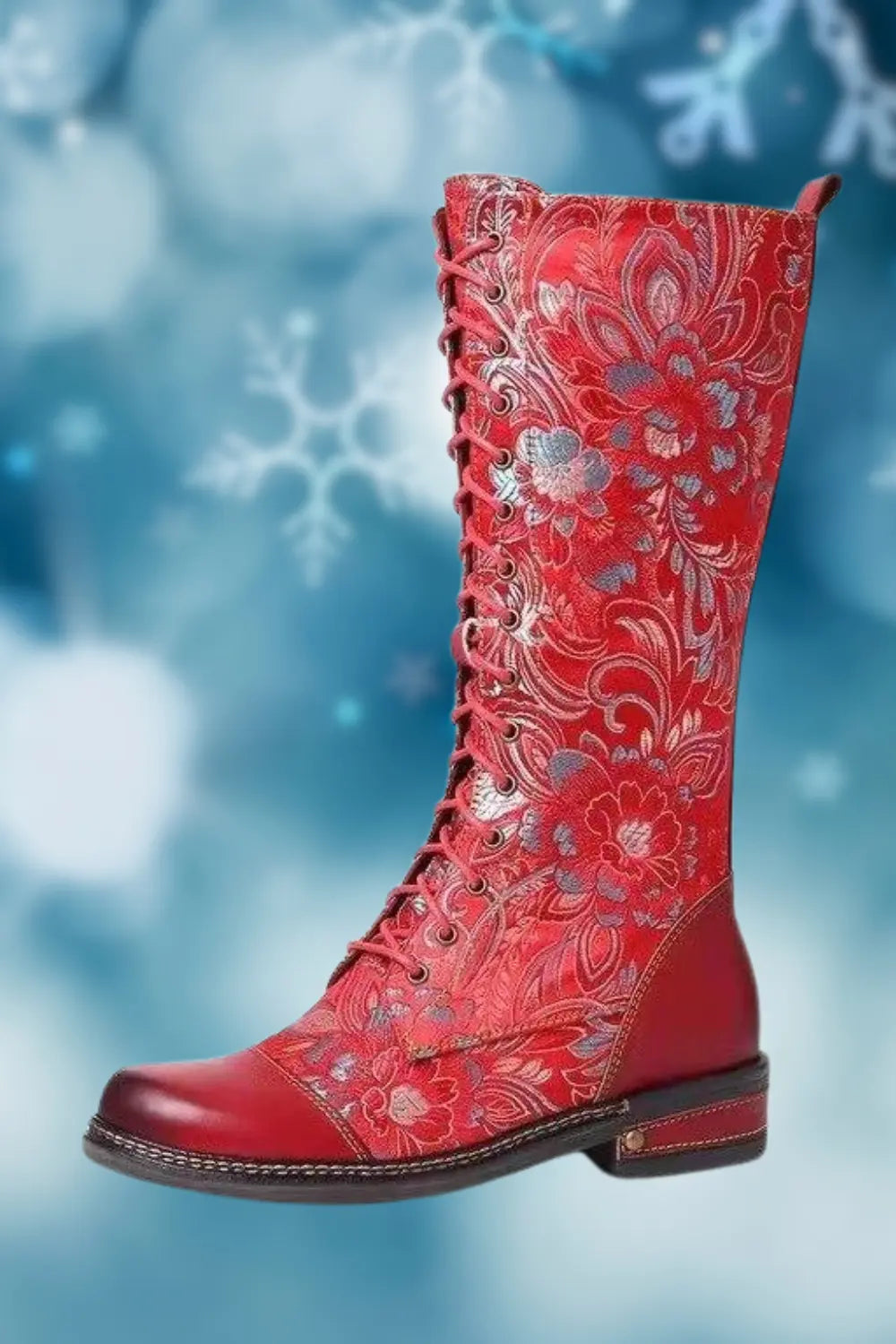 A stylish knee-high lace-up boot with a vibrant blue and red floral pattern, featuring leather accents on the toe and heel, set against a soft blue background with snowflake motifs.