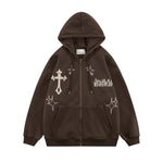 A dark brown zip-up hoodie with a relaxed fit, drawstring hood, and front kangaroo pockets. The design features white gothic-style graphics, including a large cross on the upper left side, spark-like star motifs on the chest and sleeves, and stylized text on the upper right chest for a bold streetwear look.