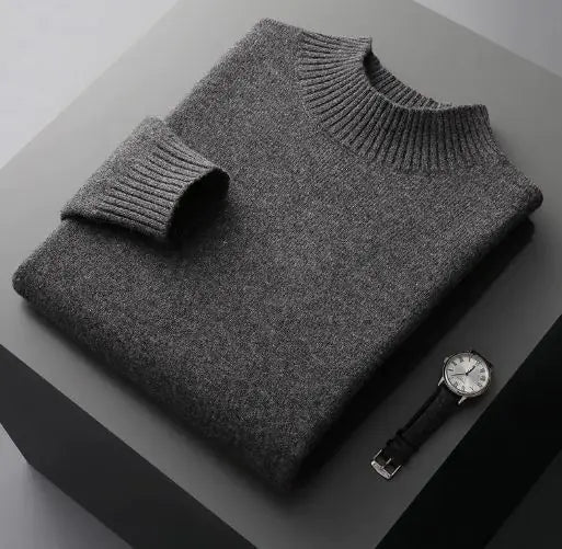 A neatly folded beige knitted sweater with a ribbed high collar and cuffs, placed on a dark grey surface. Beside the sweater, a classic wristwatch with a black leather strap and a silver dial is positioned, adding a touch of elegance to the composition.