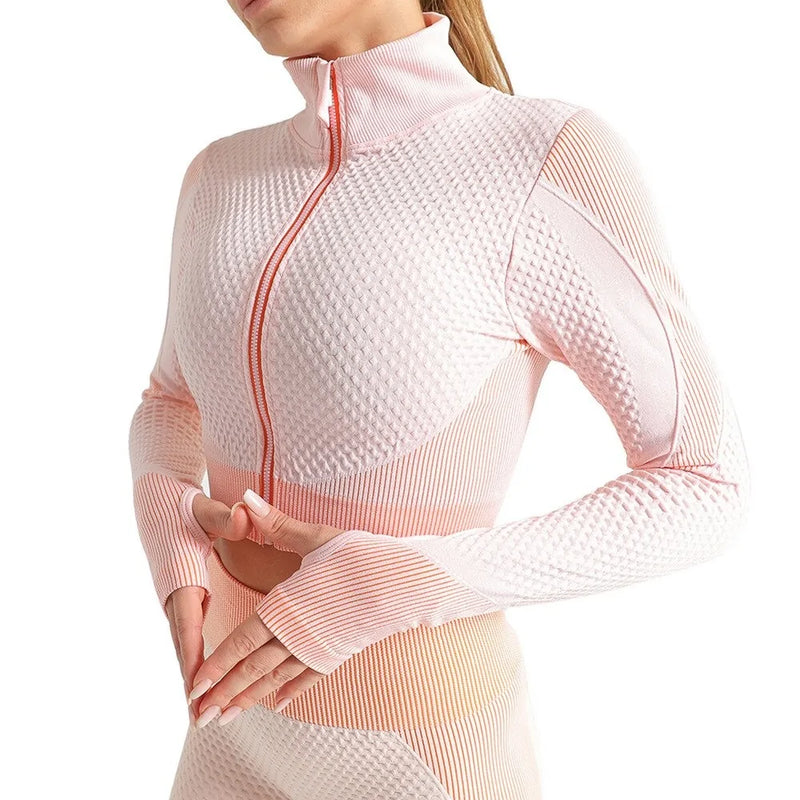 Woman wearing a seamless, textured long-sleeve athletic zip-up top in a light pink and peach gradient, featuring a high collar and thumb holes.
