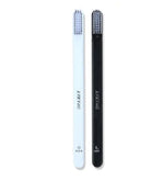 Two slim toothbrushes—one white and one black—with dense bristles, shown upright on a plain white background.