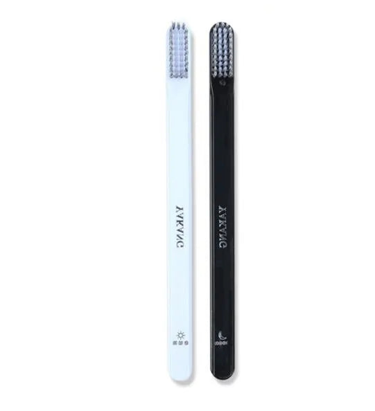 Two slim toothbrushes—one white and one black—with dense bristles, shown upright on a plain white background.