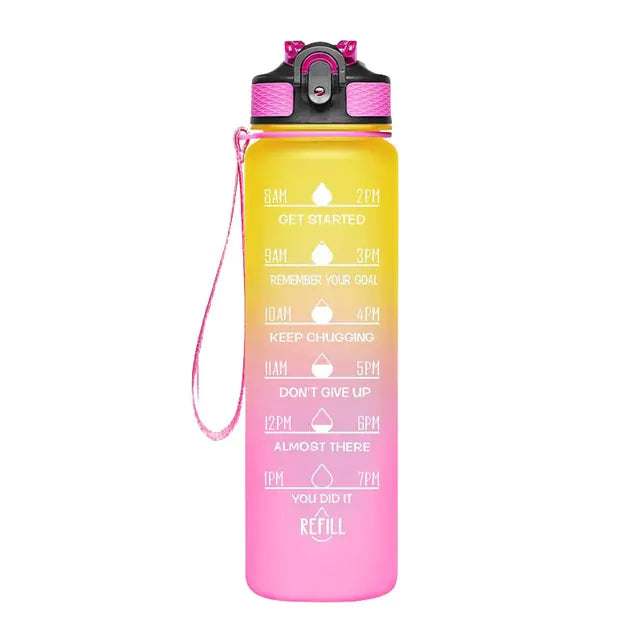 A tall motivational water bottle with a yellow-to-pink gradient, black flip-top lid, and pink wrist strap, printed with hourly drink reminders and phrases like “Get Started,” “Keep Chugging,” and “Refill.
