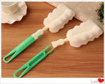 Two green-handled cleaning brushes with white, flower-shaped sponge heads lying on a wooden tabletop.