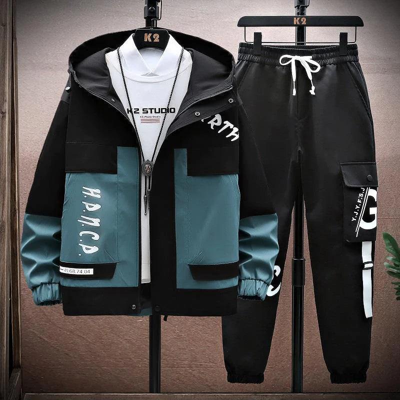 A stylish men's streetwear tracksuit set displayed on hangers. The set includes a black and teal hooded jacket with a bold, modern design, featuring large pockets, graphic text details, and a front zipper closure. The matching black jogger pants have a relaxed fit, cargo-style pockets, and white graphic text on the side, along with a drawstring waistband for adjustability. The outfit is paired with a white t-shirt and a pendant necklace, giving it a trendy, urban aesthetic.