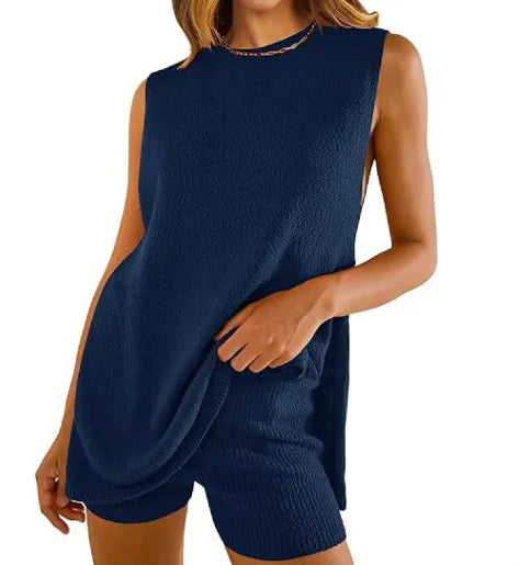 Woman standing on a sandy beach wearing a sleeveless, rust-orange mini dress with a relaxed fit and subtle ribbed texture on the sides, with the ocean and rocks in the background under a clear blue sky