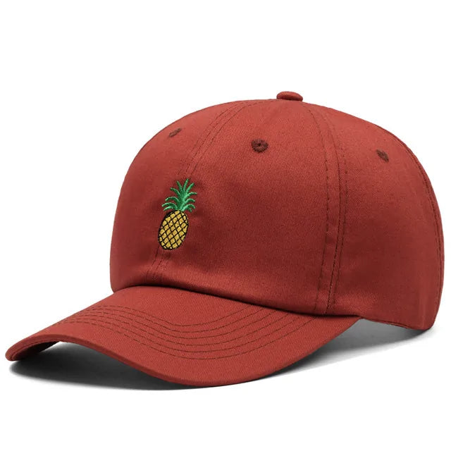 A rust-red baseball cap with a curved brim and a small embroidered pineapple logo on the front, shown on a white background.