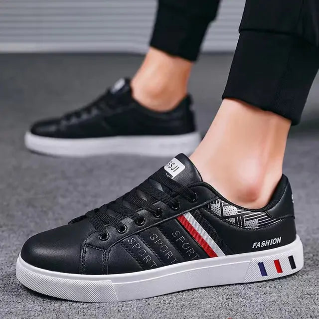 A pair of black low-top sneakers with white soles, worn by a person dressed in black joggers. The shoes feature red, white, and blue side stripes, “SPORT” lettering on the side panels, and the word “FASHION” near the heel.
