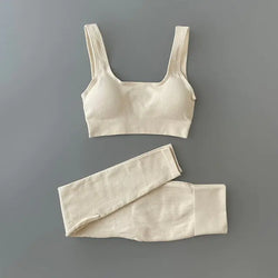 Black ribbed sports bra and matching high-waisted leggings set laid flat on a neutral gray background. The outfit is designed for activewear or athleisure, featuring a scoop neckline and wide straps on the bra.