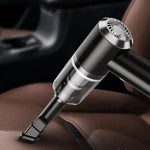 Close-up of a small handheld vacuum with a crevice tool cleaning crumbs from a brown leather car seat.