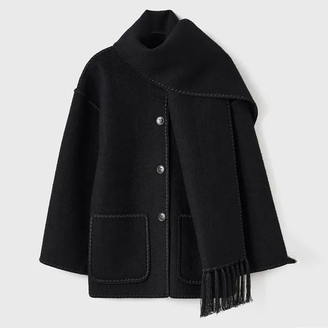 Dark wool coat with white blanket stitch trim, featuring front buttons, large patch pockets, and an attached matching scarf with fringe detailing draped over the shoulder. The coat is displayed against a plain white background.