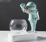 Decorative plant pot holder featuring a mint-green diver figurine beside a clear round glass bowl on a white base.