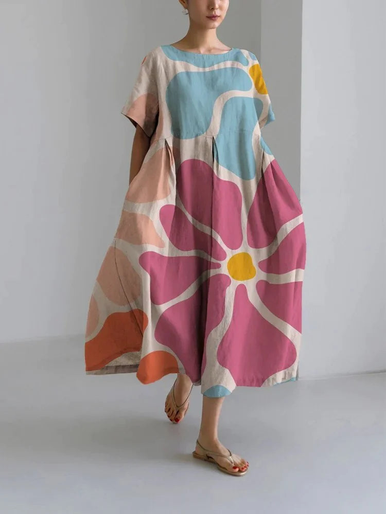 Woman wearing a loose-fitting, white midi dress with short sleeves, featuring bold red-orange floral prints accented with blue centers, paired with flat sandals.