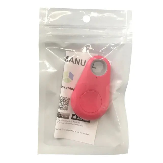 Small pink keychain tracker device with a circular button and a metal key ring, shown inside a clear resealable plastic pouch with a user manual behind it.