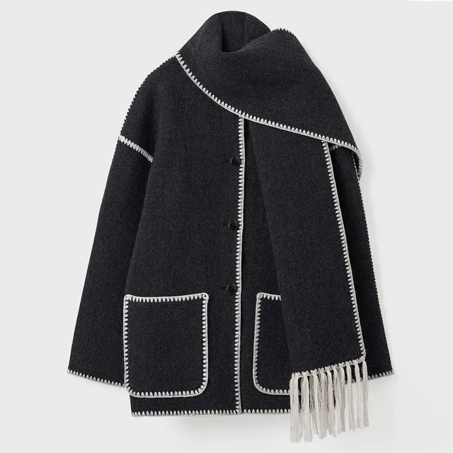 Dark wool coat with white blanket stitch trim, featuring front buttons, large patch pockets, and an attached matching scarf with fringe detailing draped over the shoulder. The coat is displayed against a plain white background.