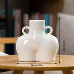 White ceramic body-shaped vase with small loop handles, shown on a wooden table with dimensions marked as 14 cm wide and 13 cm tall.