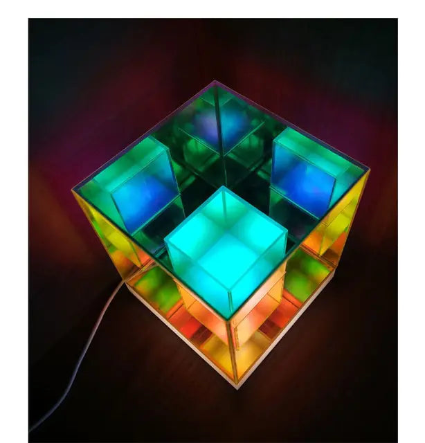 Color-changing LED cube lamp with translucent, layered square compartments glowing in blue, green, and orange, shown from above with a power cord on a dark background.