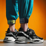 Black chunky trainers with white platform soles and grey strap details, worn with teal joggers.
