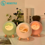 Three round bedside night lights with short wooden legs, glowing in green, white, and pink, each featuring a sleeping bird design inside the center window.